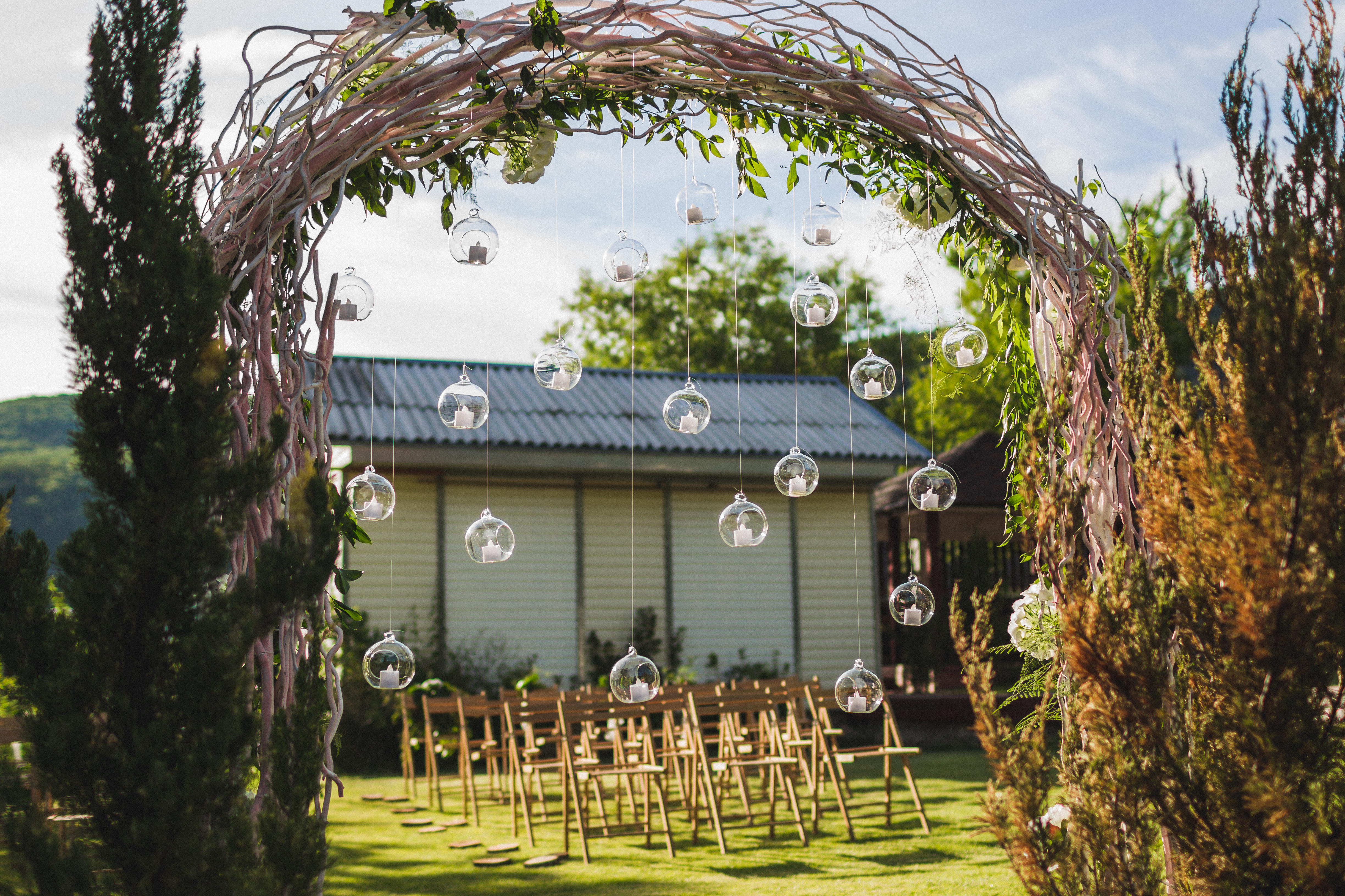 Evening wedding ceremony in garden, arch with white branches, brown wooden chairs